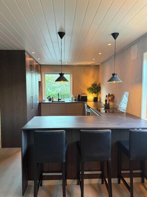 Una cocina moderna con una isla central, luces colgantes y vistas al exterior.