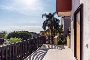 Ein Balkon mit Blick auf das Meer, eine Palme und ein Gebäude mit rotem Dach.