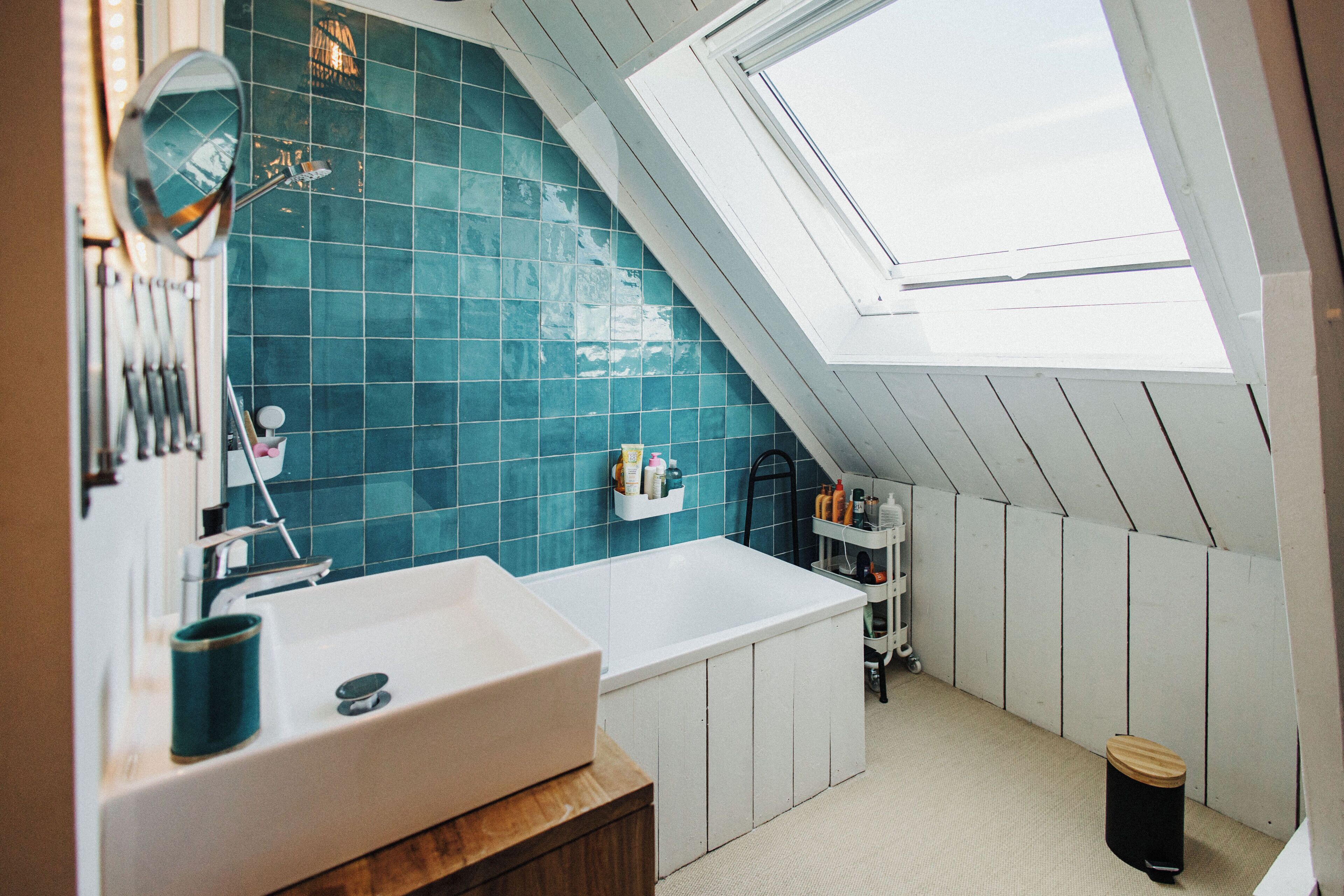 A bathroom with a skylight, a sink, a mirror, and a shelf with toiletries.