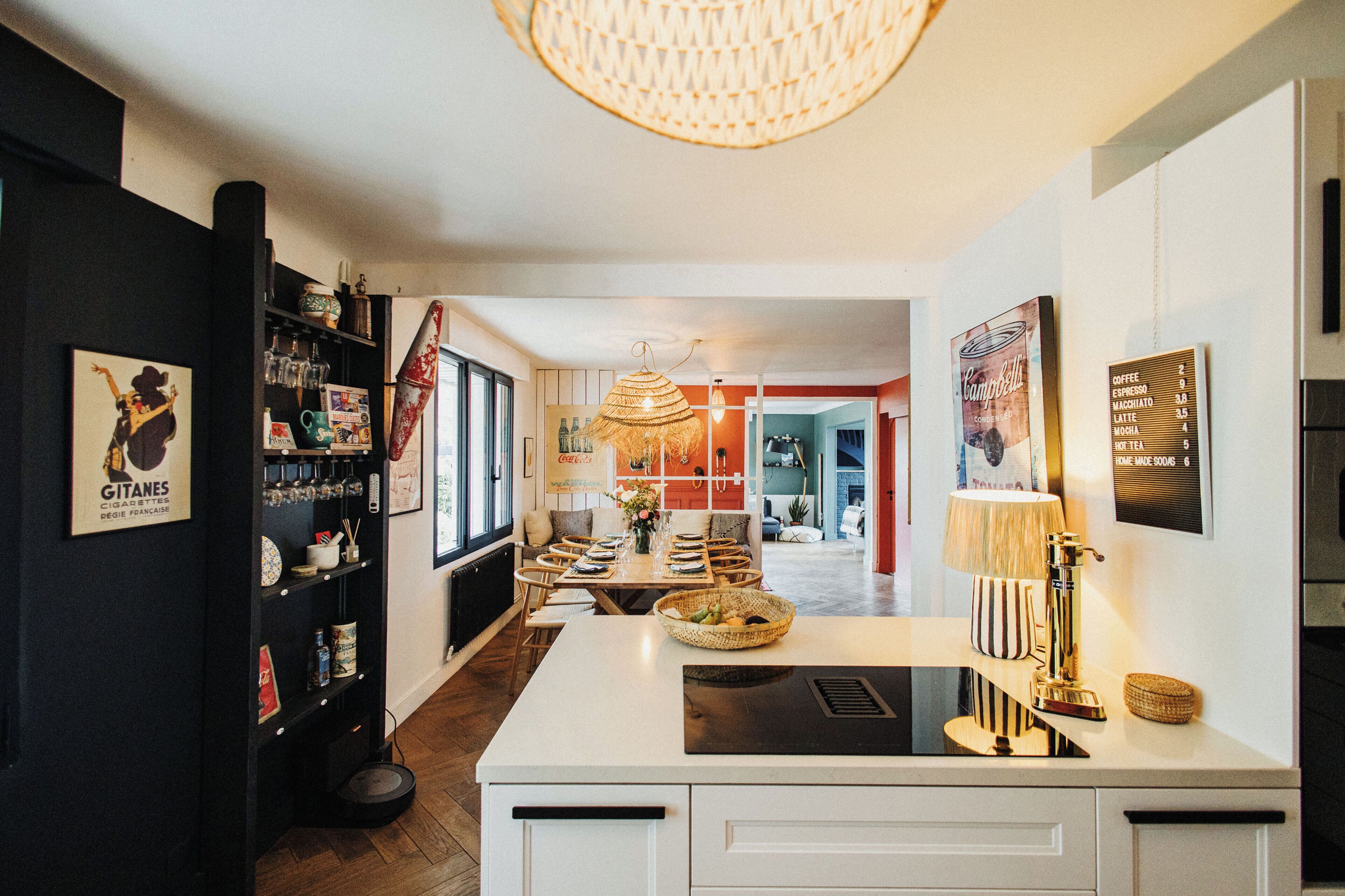 A modern kitchen with a central island, a dining area with chairs, and a hanging light fixture.