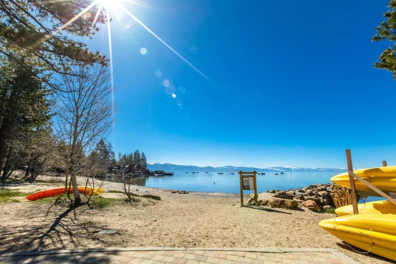En strand med kajaker, en träbänk och en fri utsikt över sjön och bergen.