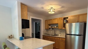 Una cocina con armarios de madera, un refrigerador de acero inoxidable, encimera de mármol y una silla tapizada en tono verde.
