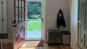 Una habitación con piso de madera, puerta de vidrio corredera que da a una zona verde y un armario pequeño junto a un perchero.
