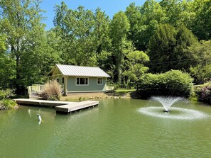 Uma cabana à beira do lago, com um cais e uma fonte.