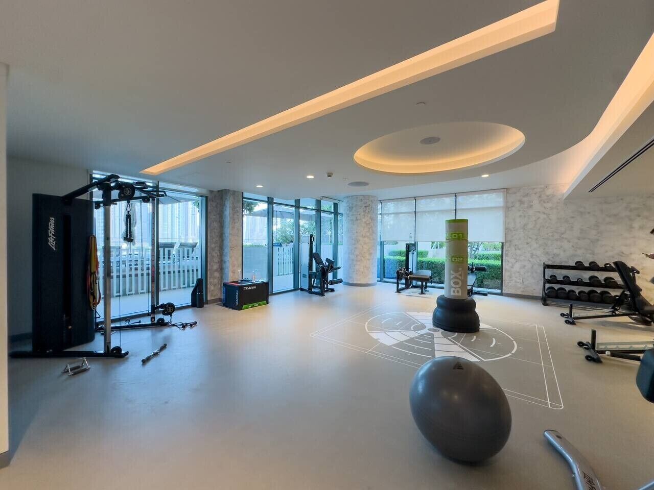 Uma academia espaçosa com diversos equipamentos de ginástica, grandes janelas e design moderno.