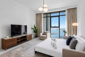 A modern hotel room with a large bed, a TV, a sofa, a coffee table, and a view of the sea. - Sophisticated Sea View Retreat At Emaar Beachfront (Dubai)