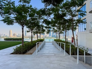 A pathway leading to a building with a view of a city skyline and water. - Sophisticated Sea View Retreat At Emaar Beachfront (Dubai)