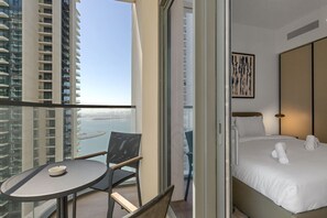 A hotel room with a bed, a chair, a small table, and a view of the cityscape and water. - Sophisticated Sea View Retreat At Emaar Beachfront (Dubai)