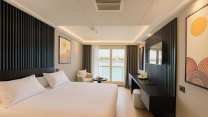 Ein Hotelzimmer mit einem großen Bett, einem Schreibtisch, einem Stuhl, einem kleinen Tisch, einem Spiegel und Blick ins Freie.