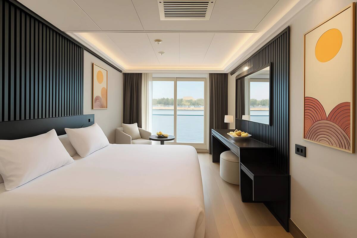 Ein Hotelzimmer mit einem großen Bett, einem Schreibtisch, einem Sessel, einem kleinen Tisch und Blick auf ein Gewässer.