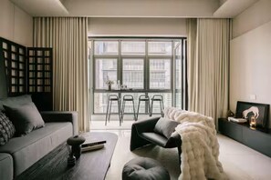 A modern living room with a sofa, a coffee table, a chair, a large window with curtains, and a TV stand with a picture frame. - Chic Cityscape Stay in Bukit Bintang, TRX | 1-6pax (Kuala Lumpur)