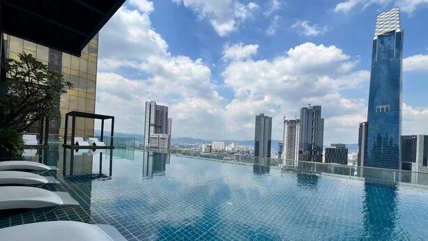 Ein Infinity-Pool auf dem Dach mit Blick auf die Stadtlandschaft, moderne Gebäude und einen klaren Himmel.