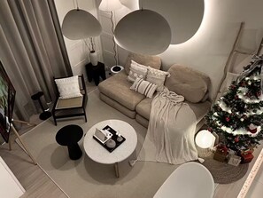 A modern living room with a sofa, a round coffee table, a chair, a small table with a lamp, and a Christmas tree. - Comfy Loft in EkoCheras, Link to MRT | 1-6 pax (Kuala Lumpur)