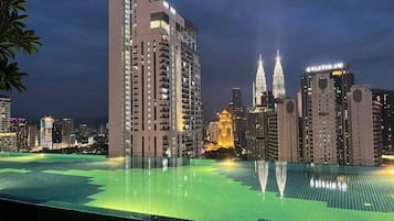 A high-rise hotel with a rooftop infinity pool, a prominent building with a spire, and the Petronas Twin Towers in the background.