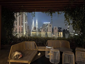 A rooftop terrace with a view of the city skyline, including the Petronas Towers, and furnished with wicker seating and metal stools. - Cozy Cityscape Stay in KLCC, Quill Mall | 1-5 pax (Kuala Lumpur)