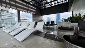 A rooftop lounge with white lounge chairs, a wicker chair, and a view of the city skyline. - Rare Cityscape Stay in Bukit Bintang, TRX | 1-6pax (Kuala Lumpur)