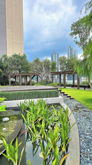 A landscaped garden with a pond, seating areas, and modern buildings in the background. - Rare Cityscape Stay in Bukit Bintang, TRX | 1-6pax (Kuala Lumpur)
