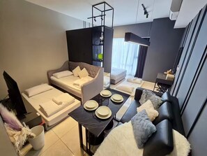 Een moderne hotelkamer met een bank, een bed, een eettafel met borden en een groot raam.