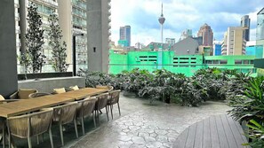 An outdoor seating area with a wooden table and chairs, surrounded by greenery and a cityscape view. - Rare Cityscape Stay in Bukit Bintang, TRX | 1-6pax (Kuala Lumpur)