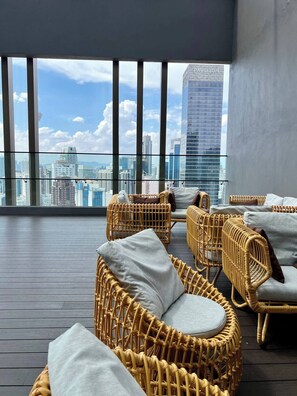 Een balkon met rieten meubilair, uitzicht op de stad en een modern gebouw met de tekst 'PAVILTON'.