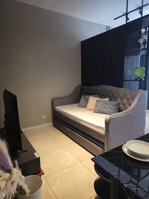 Een moderne woonkamer met een bank, een flatscreen televisie, een bijzettafeltje en een decoratieve plant.