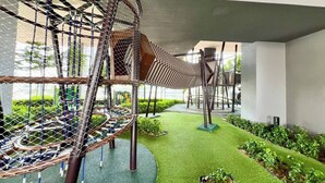 Ein Spielplatz mit einer Seilbrücke, einer runden Kletterkonstruktion und Rasen aus Kunstgrün.