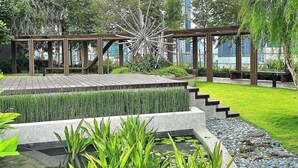 Ein angelegter Garten mit Teich, Sitzbereichen und modernen Gebäuden im Hintergrund.