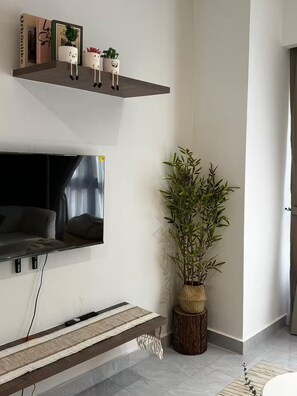 Een moderne woonkamer met een flatscreen televisie, een houten plank met decoratieve spullen, een grote bamboeplant en een geweven vloerkleed.