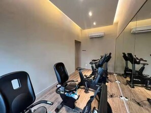 Een sportschool met trainingsfietsen en een stoel, een spiegel aan de muur en een airconditioner.