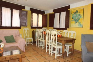 Zona pranzo con tavolo in legno e sedie bianche, un divano e un quadro appeso al muro.