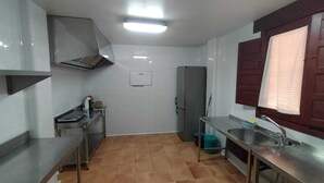 A compact kitchen with a stainless steel countertop, a built-in oven, a refrigerator, and a window with wooden shutters. - House for 16 next to Burgo de Osma.  Hiking, wine, castles. Pets (Alcubilla del Marqués)