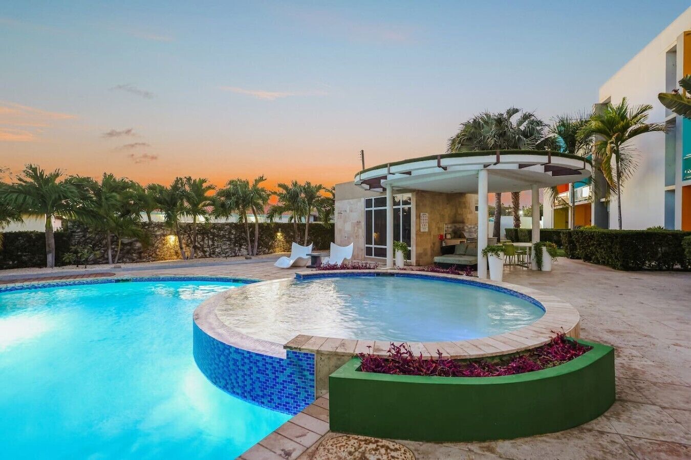 Ein Pool mit einer eingelassenen Sitzecke, umgeben von Palmen und einer überdachten Lounge.