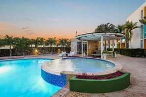 Ein Pool mit einer eingelassenen Sitzecke, umgeben von Palmen und einer überdachten Lounge.