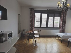 A room with a wooden floor, a bed, a table with chairs, a TV, and a window with curtains. - Mozart Studios (Cluj-Napoca)