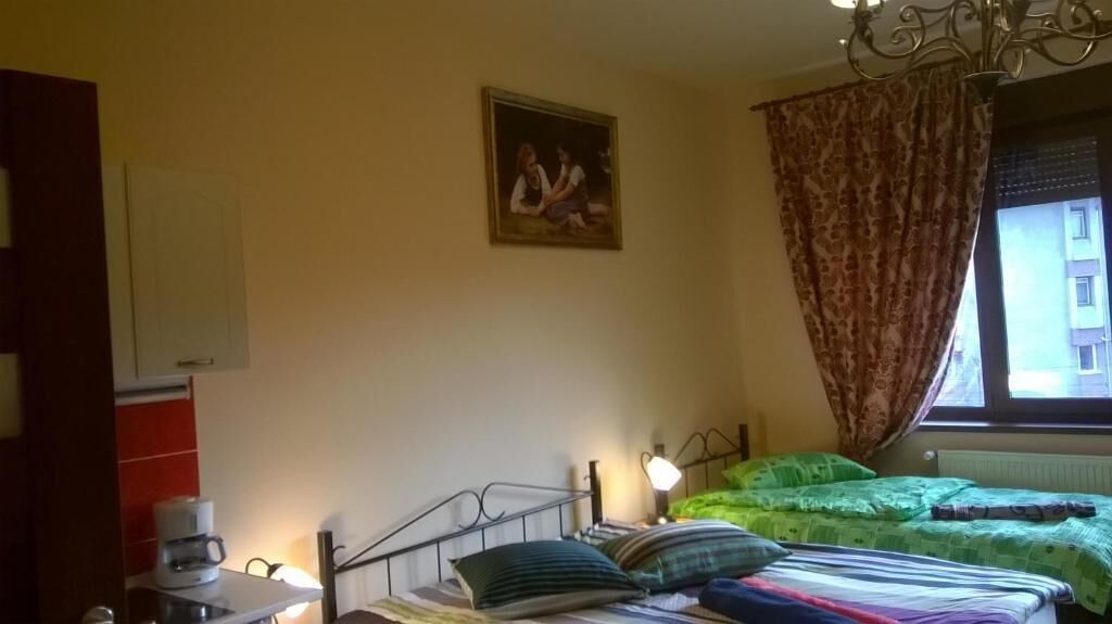 A bedroom with a bed, a bedside table with a lamp, a window with curtains, and a painting on the wall.