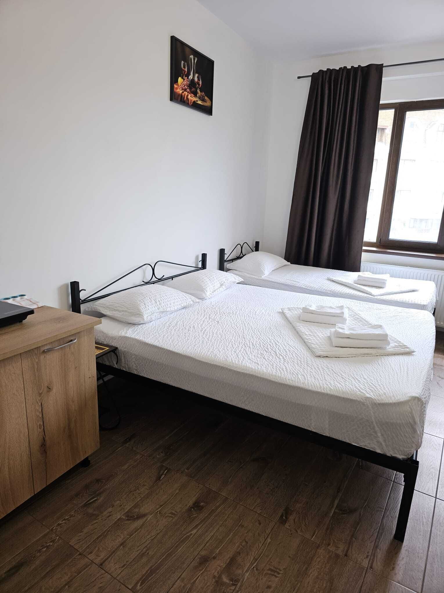 A hotel room with two beds, a wooden dresser, a painting on the wall, and a window with curtains.