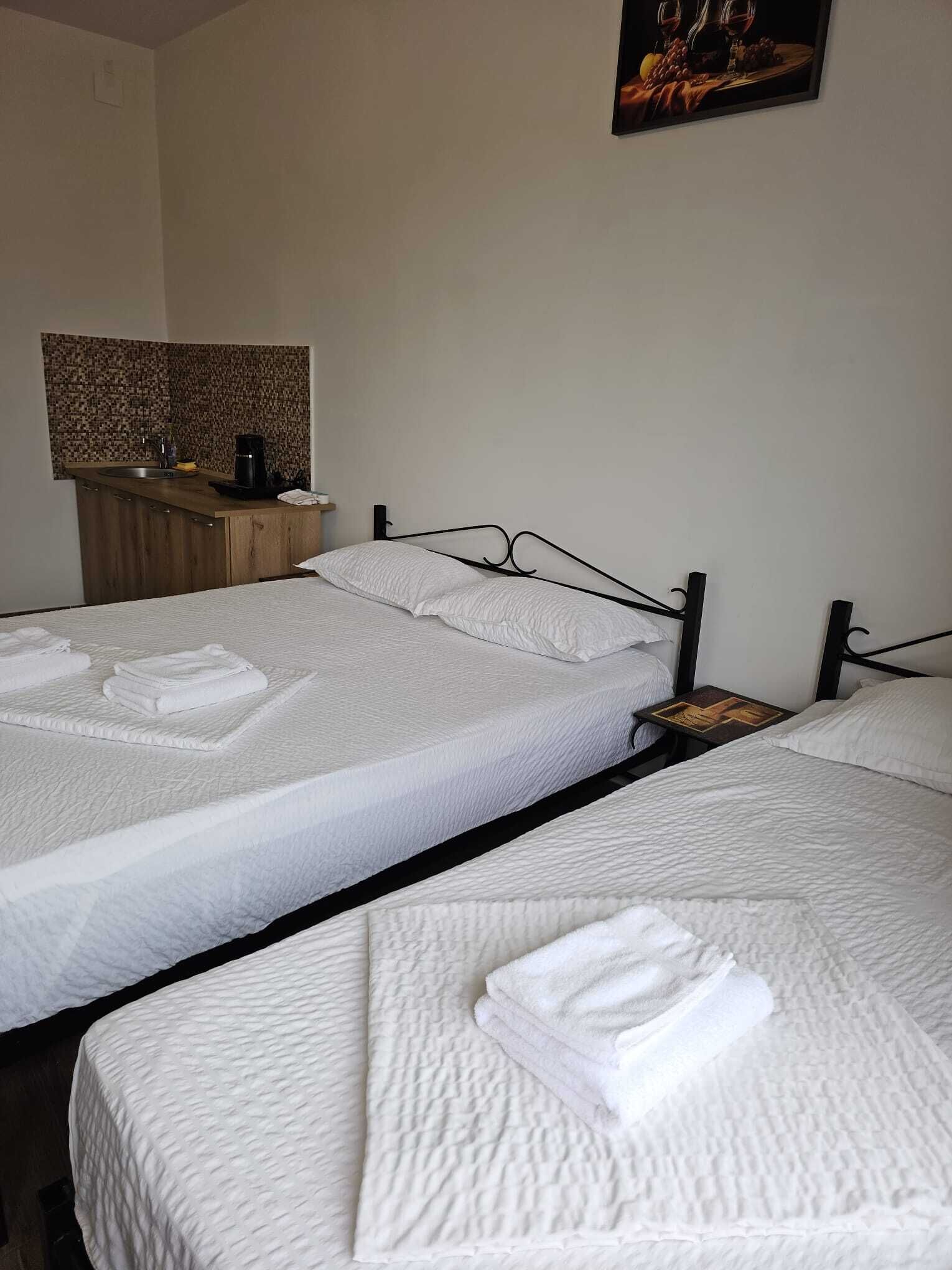A hotel room with two beds, a small table, a sink, and a painting on the wall.