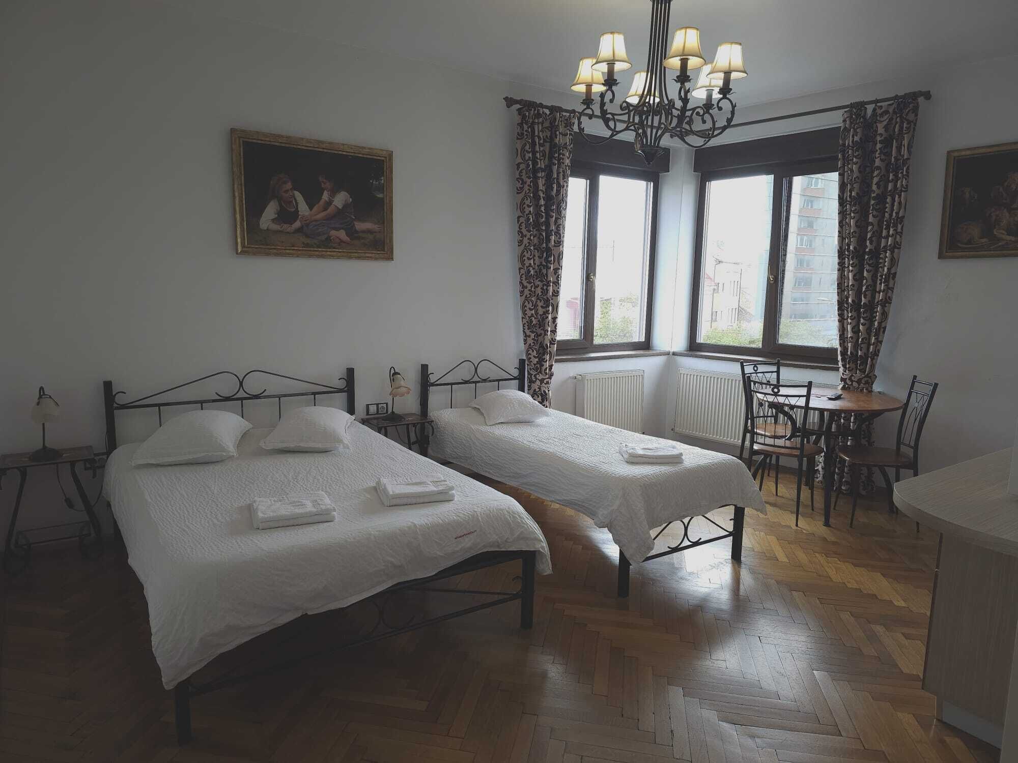 A hotel room with two beds, a dining table, a chandelier, and a painting on the wall.