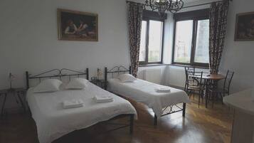 A hotel room with two beds, a dining table, a chandelier, and a painting on the wall.