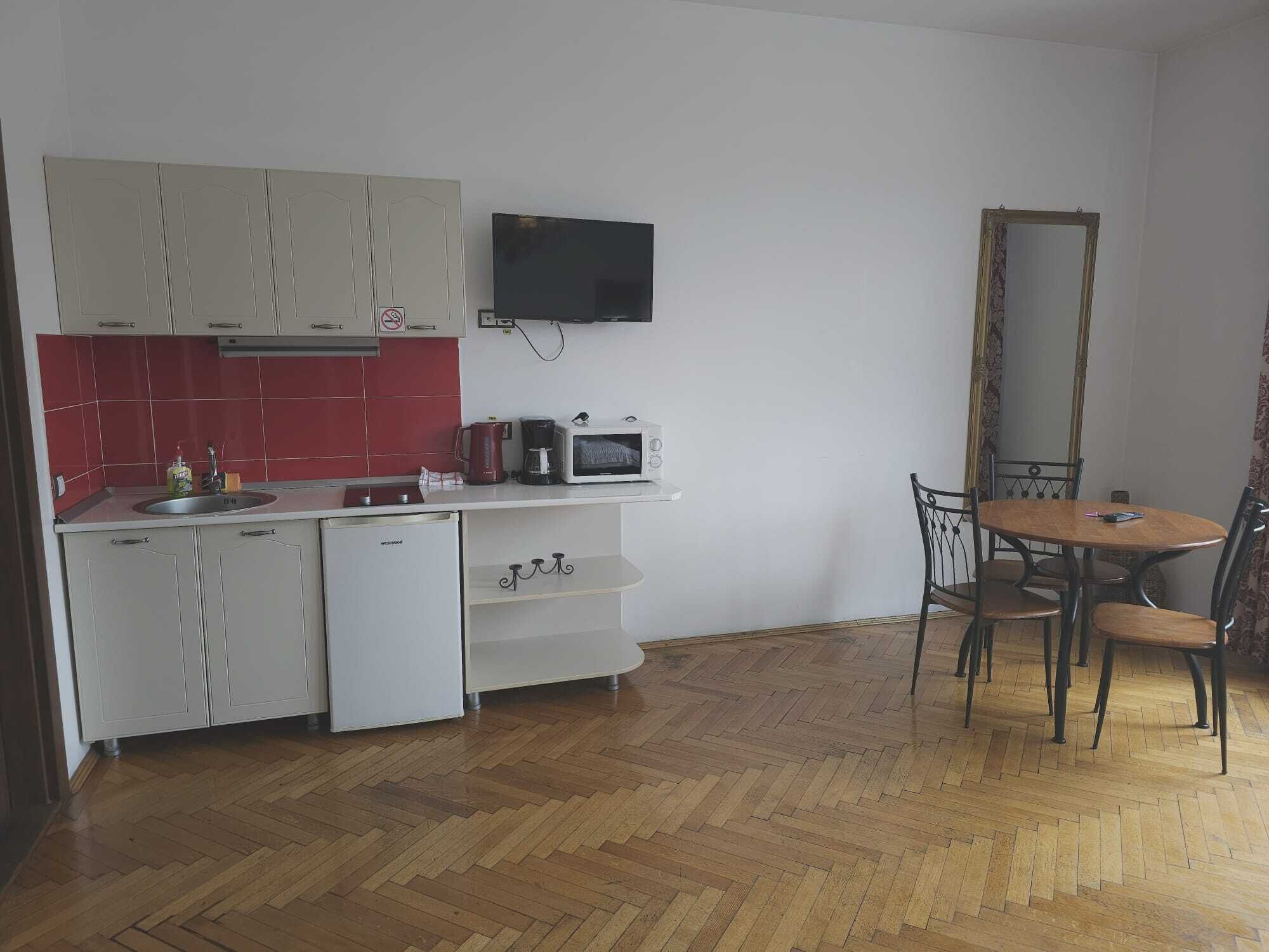 A compact kitchen with white cabinets, a red-tiled backsplash, a microwave, a coffee maker, and a dining area with a table and chairs.