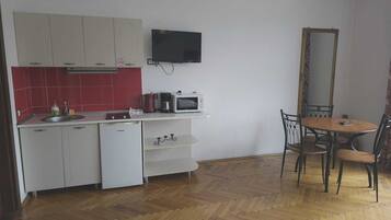 A compact kitchen with white cabinets, a red-tiled backsplash, a microwave, a coffee maker, and a dining area with a table and chairs.