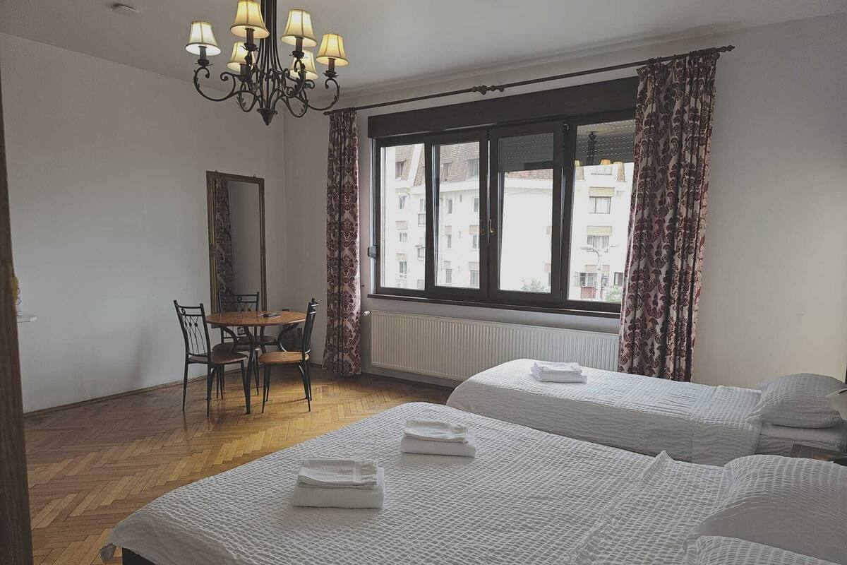 A hotel room with two beds, a desk, a chair, a mirror, and a window with curtains.