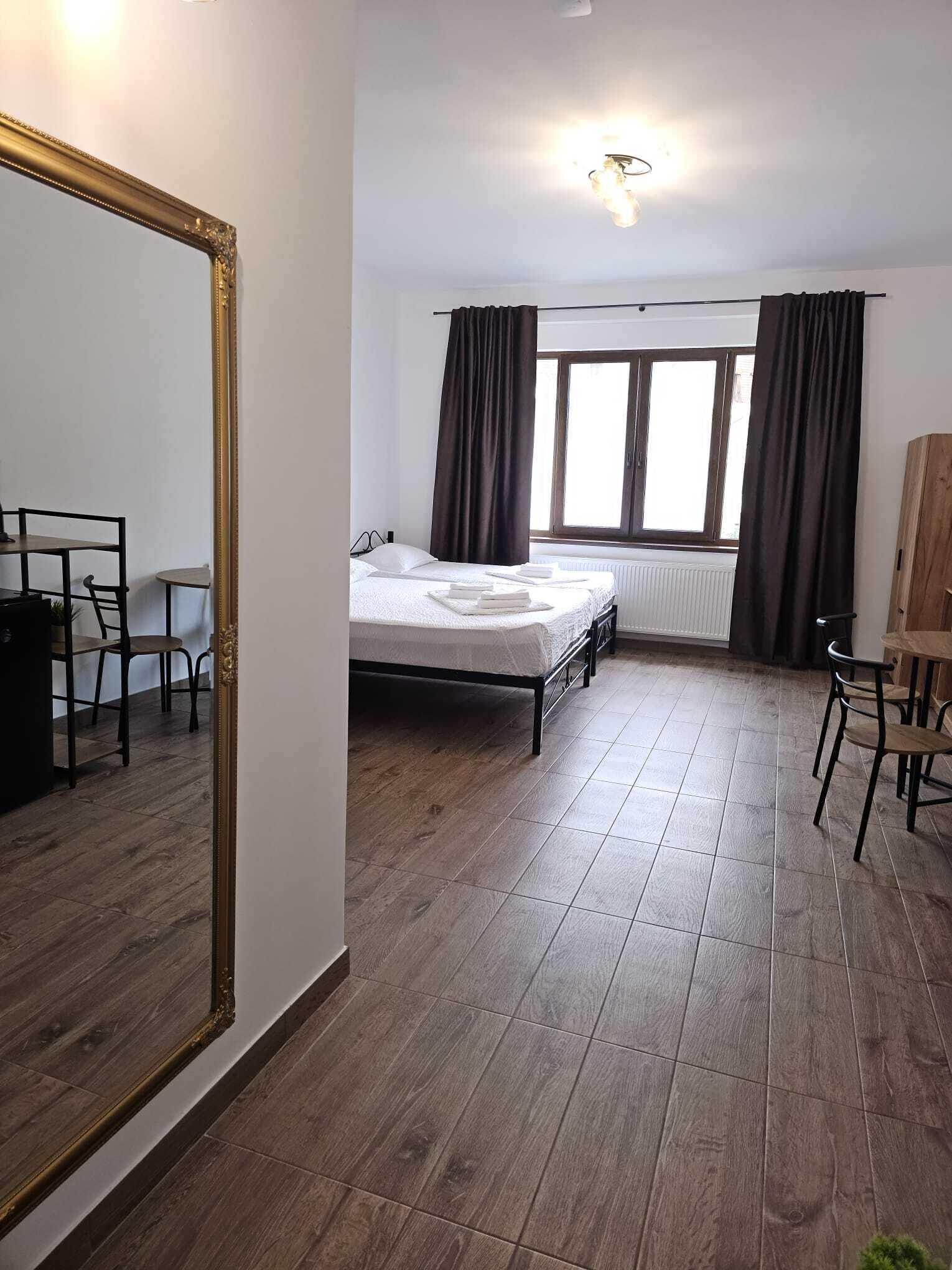 A room with a bed, a desk, a chair, a large mirror, and a window with curtains.