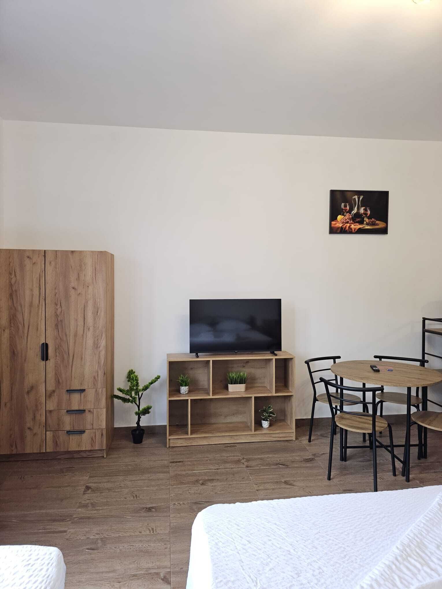 A room with a bed, a TV on a wooden stand, a dining table with chairs, and a wardrobe.