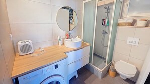 Un baño funcional con lavadora, lavamanos, espejo, ducha e inodoro.