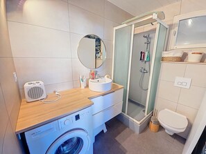 Un baño funcional con lavadora, lavamanos, espejo, ducha e inodoro.