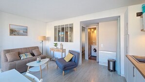 Un espacio habitable compacto con sofá, sillón, mesita y vistas a una lavadora al fondo.