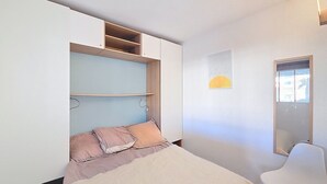 Un dormitorio con una cama, una silla y un armario con estantes.