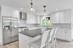 A modern kitchen with white cabinets, stainless steel appliances, a granite countertop, and pendant lighting.
