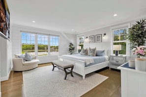 A bedroom with a large window, a bed, a bench, and a nightstand.